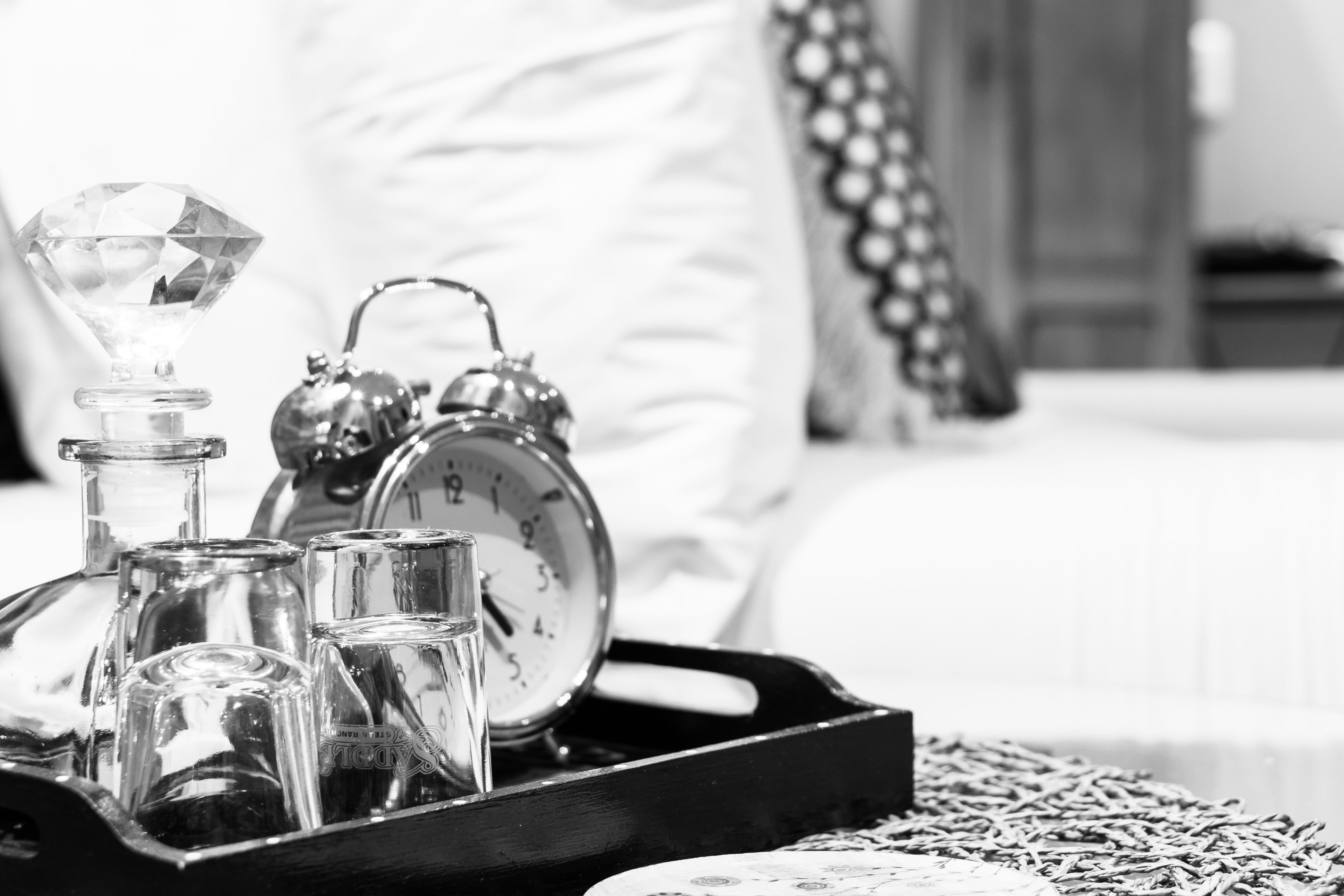 A tray with a diamond-shaped object, a clock, and several glasses on a bed.