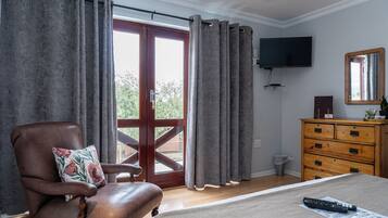 Une chambre à coucher avec un lit, une commode en bois, un téléviseur fixé au mur et une vue sur l’extérieur, visible à travers une porte vitrée.