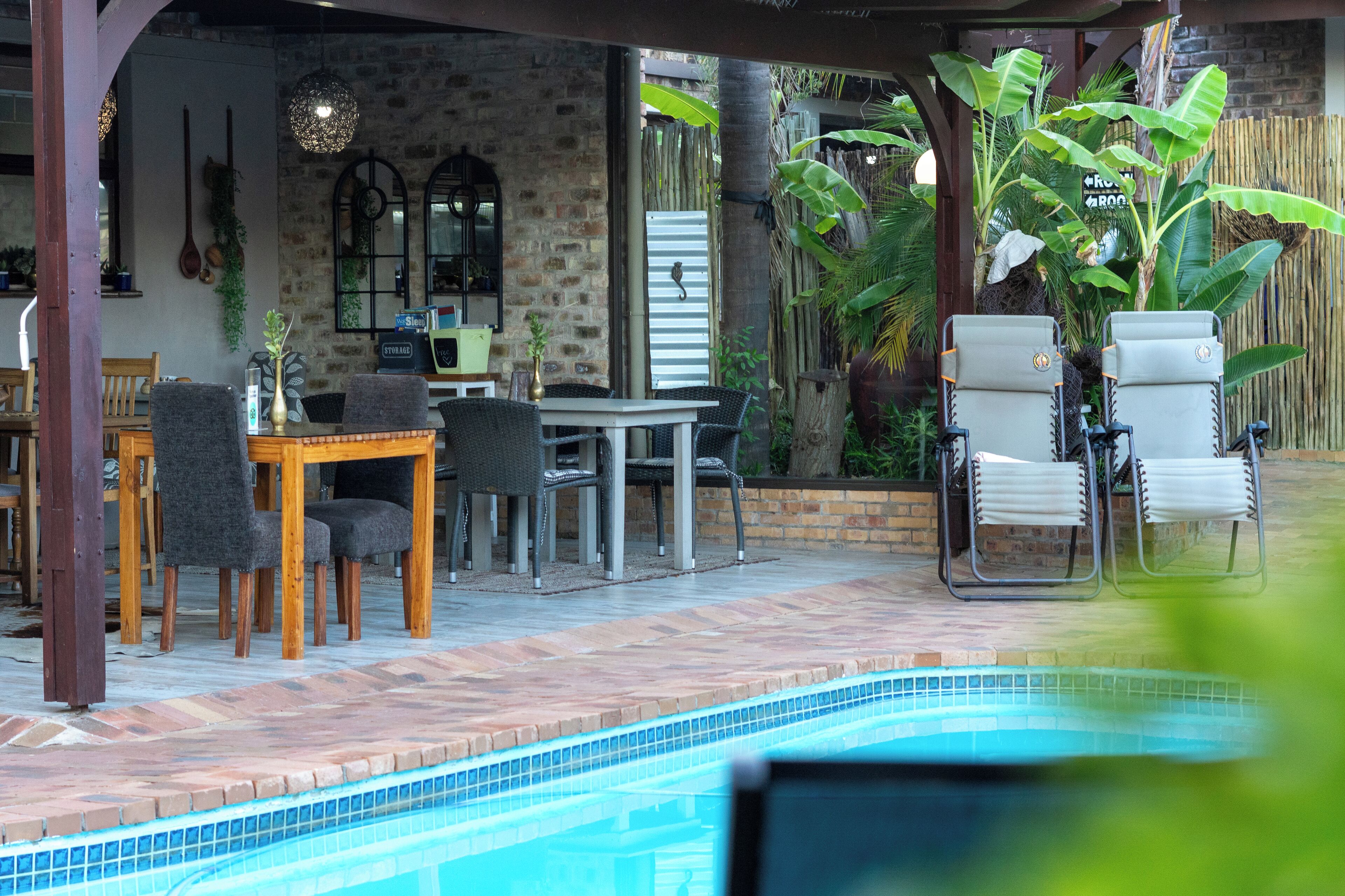 A poolside area with a dining table and chairs, a pool, and a covered seating area with chairs and a table.