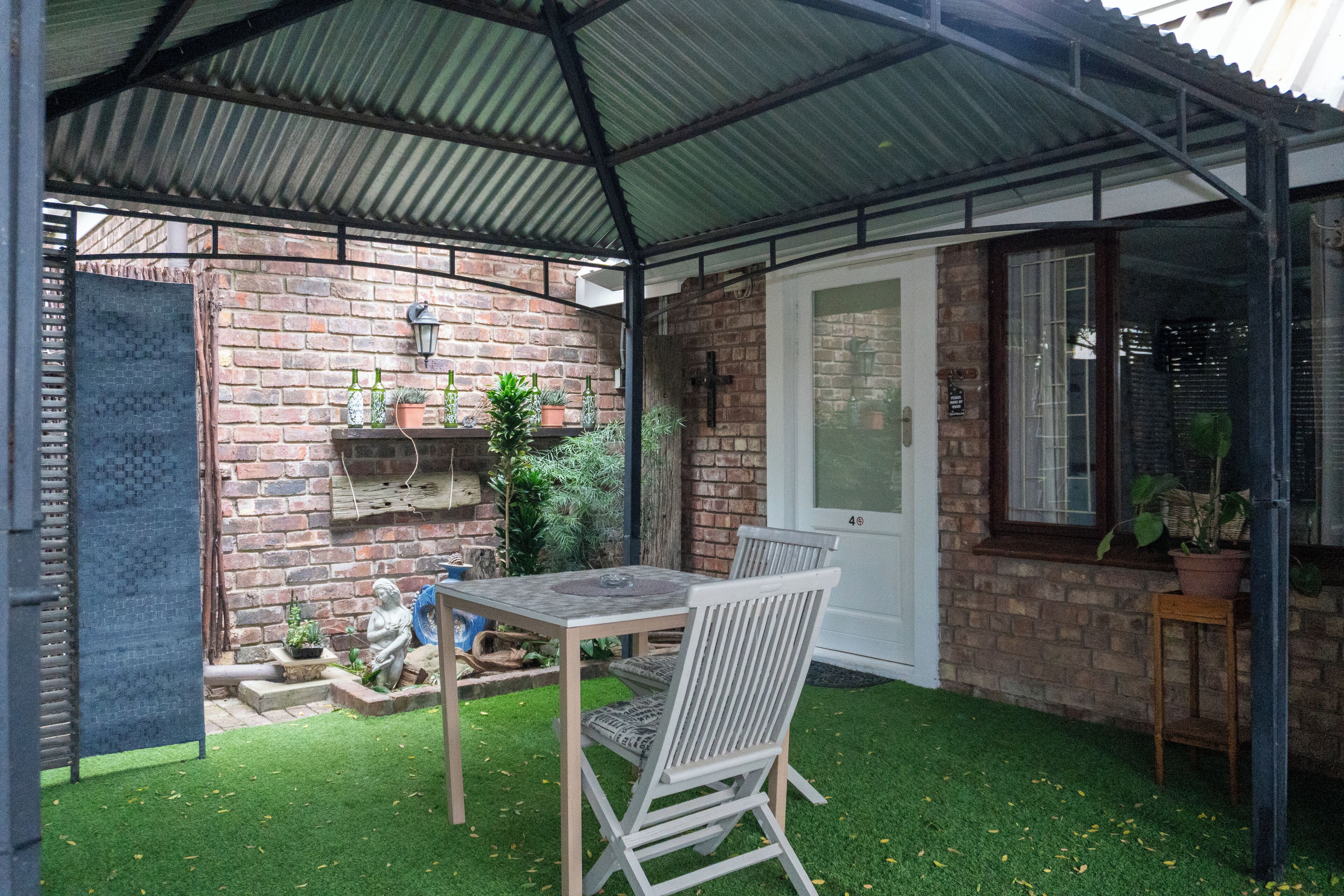A covered patio with a brick wall, a table, chairs, and potted plants.