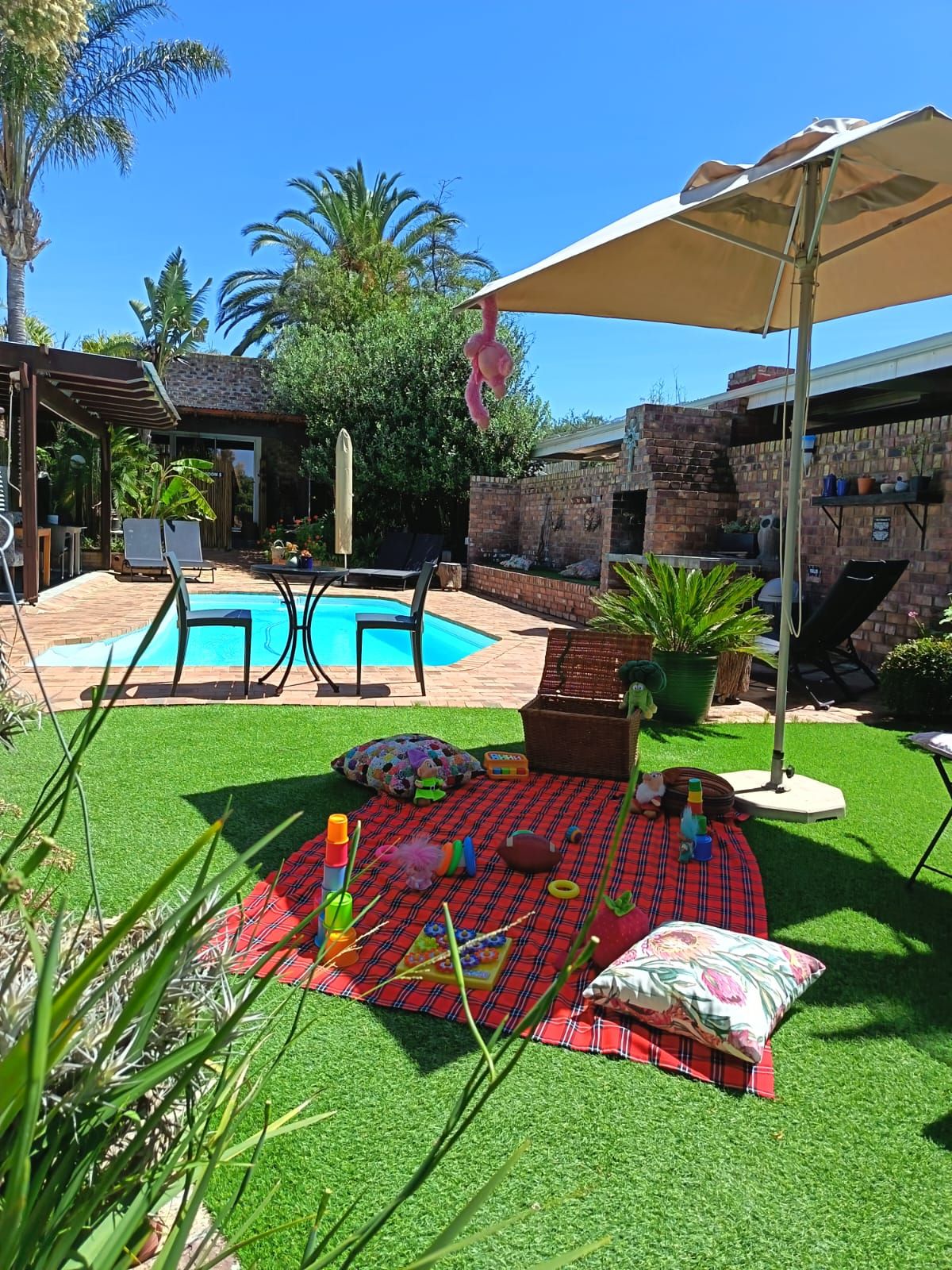 A backyard with a swimming pool, a patio area with chairs, and a covered seating area.