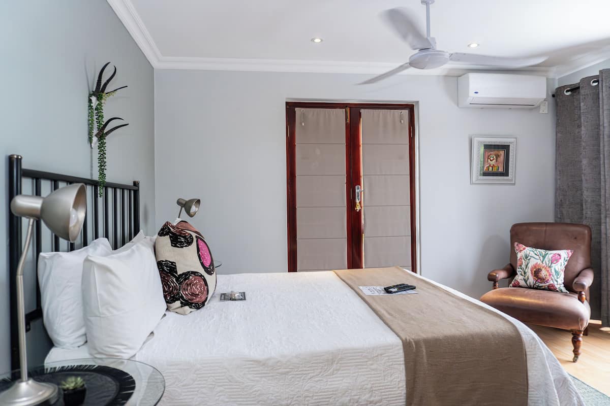 A bedroom with a bed, a chair, a desk, a ceiling fan, and a door.