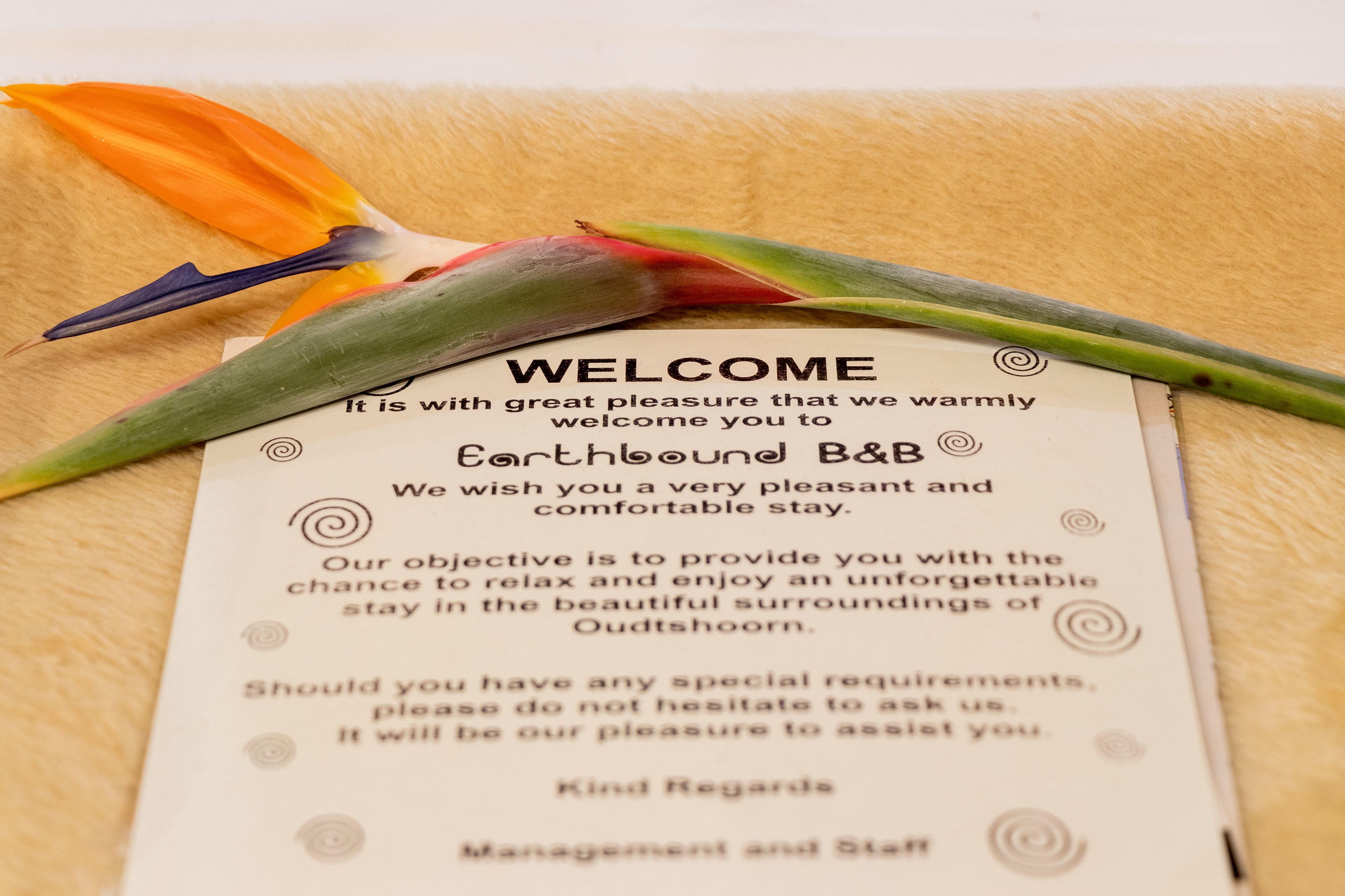 A welcome card with text welcoming guests to Earthbound B&B, mentioning a pleasant stay and surroundings of Oudtshoorn.