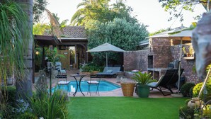 Un jardin avec une piscine, des chaises longues et un espace barbecue en briques.