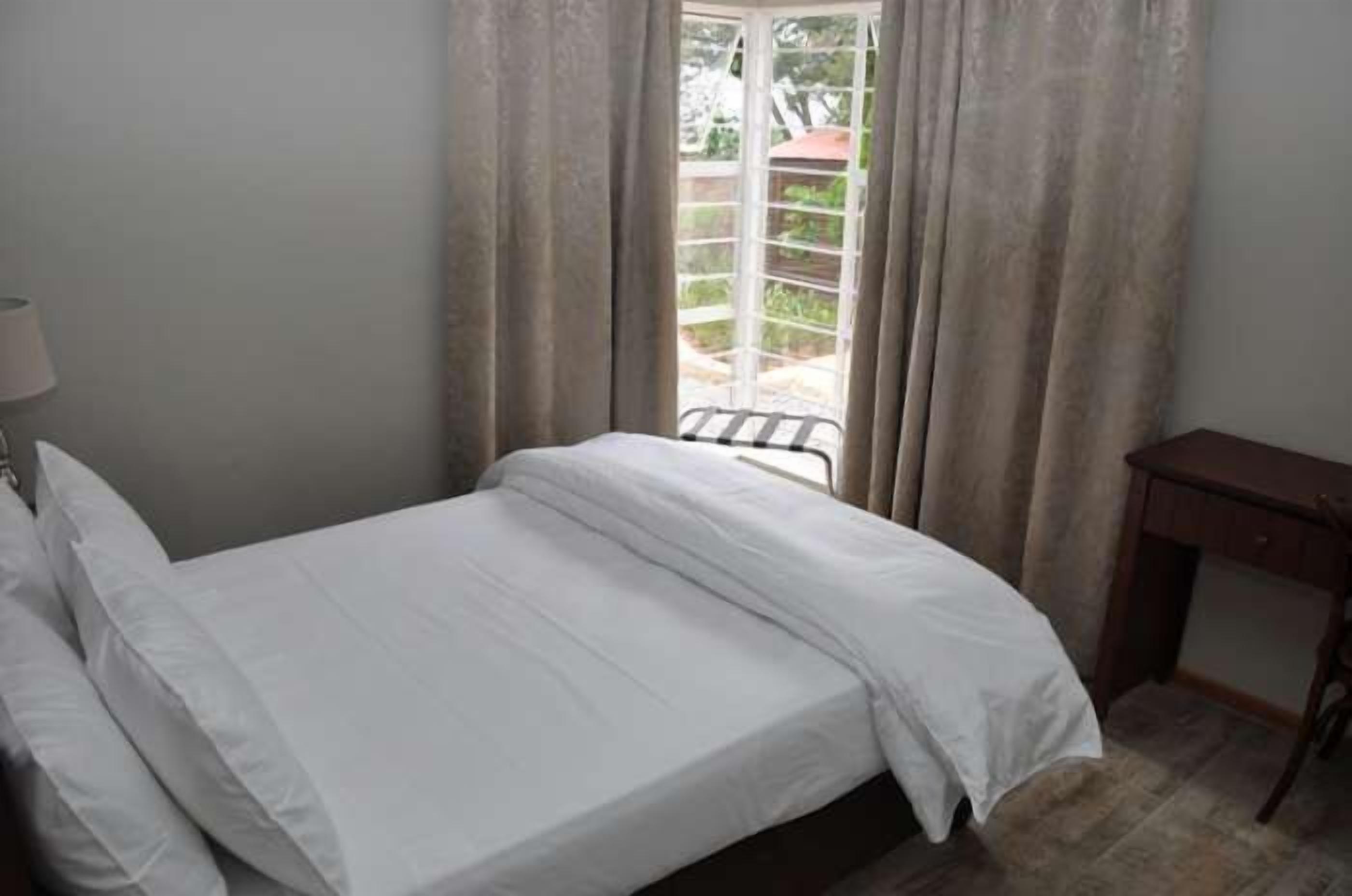 Un dormitorio con cama, escritorio y ventana con cortinas.