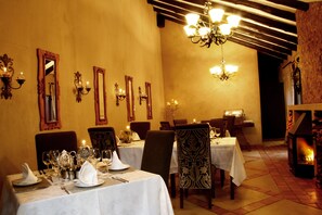 Comedor con mesas dispuestas para una comida, sillas, espejos en la pared y una chimenea.