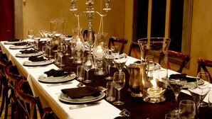 A long dining table set with multiple wine glasses, plates, and cutlery, surrounded by chairs.