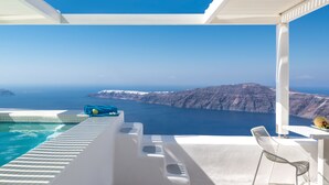 A balcony with a pool, a chair, and a view of the sea and mountains. - White Santorini (Santorini)