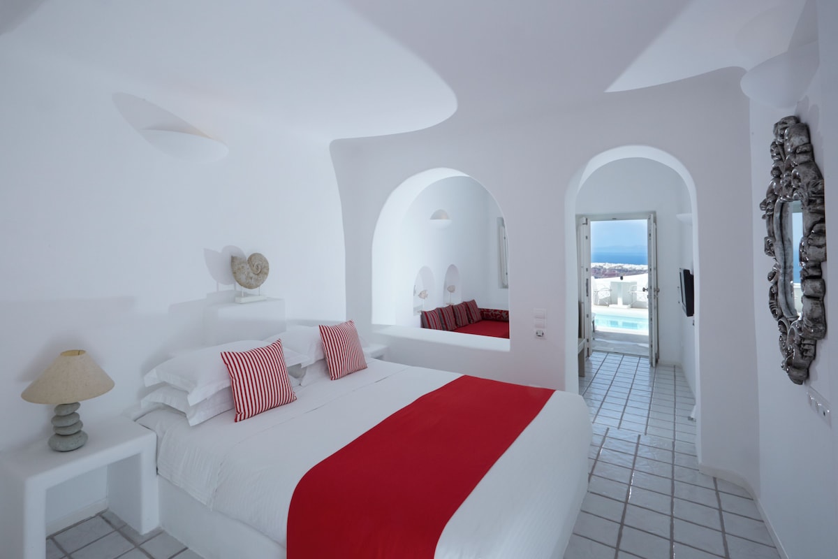 A hotel room with a bed, a nightstand, a lamp, a mirror, and a view of the sea.