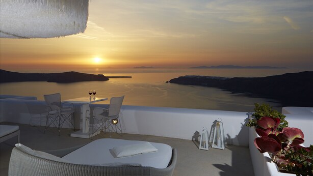 A sunset view from a balcony with a table, chairs, and a bed. - White Santorini (Santorini)