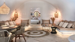 A modern interior with a round dining table, cushioned seating, and a central bed area. - White Santorini (Santorini)