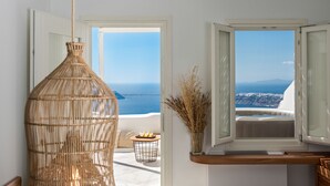 A room with a wicker vase, a small round table with a candle, and a view of the sea through an open window. - White Santorini (Santorini)