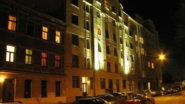 A multi-story building with illuminated windows and a parking area with cars. - Jakob Lenz Guesthouse (Riga)
