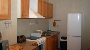 A compact kitchen with wooden cabinets, a microwave, a toaster, and a refrigerator. - Jakob Lenz Guesthouse (Riga)