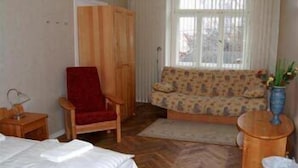 A room with a bed, a red chair, a patterned sofa, a wooden cabinet, and a window with curtains. - Jakob Lenz Guesthouse (Riga)
