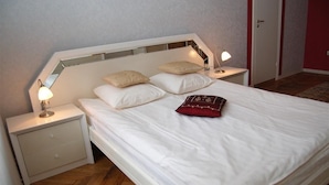 A neatly made bed with white linens and two pillows, a bedside lamp, and a small drawer unit. - Jakob Lenz Guesthouse (Riga)