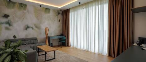 Una sala moderna con sofá, mesa de centro y escritorio. Hay un ventanal con cortinas, una planta y una pared con diseño texturizado.