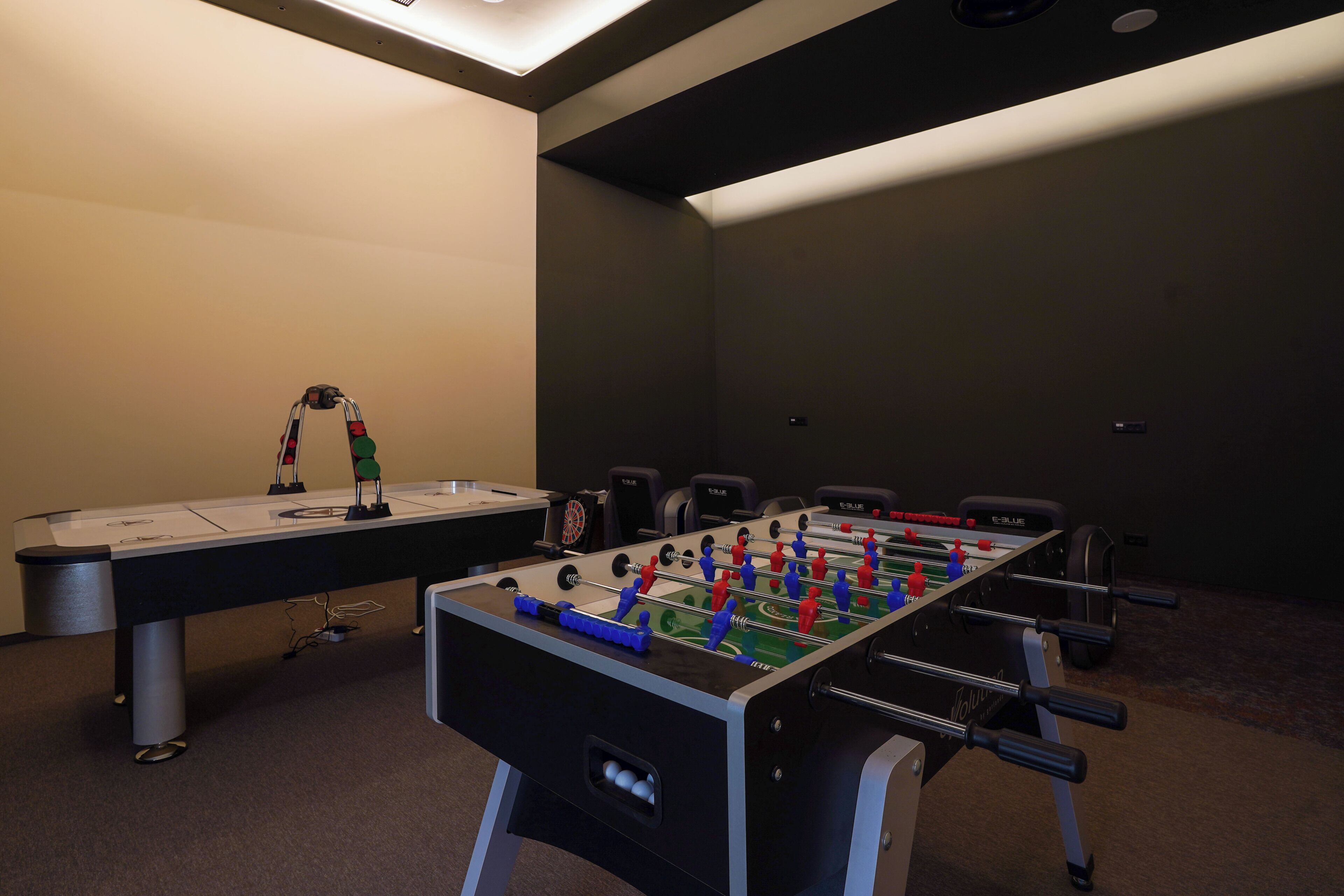 A foosball table in a room with a carpeted floor, a desk, and chairs.