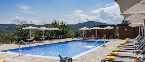 Un área junto a la piscina con sillones de descanso, sombrillas y una vista despejada de las montañas.