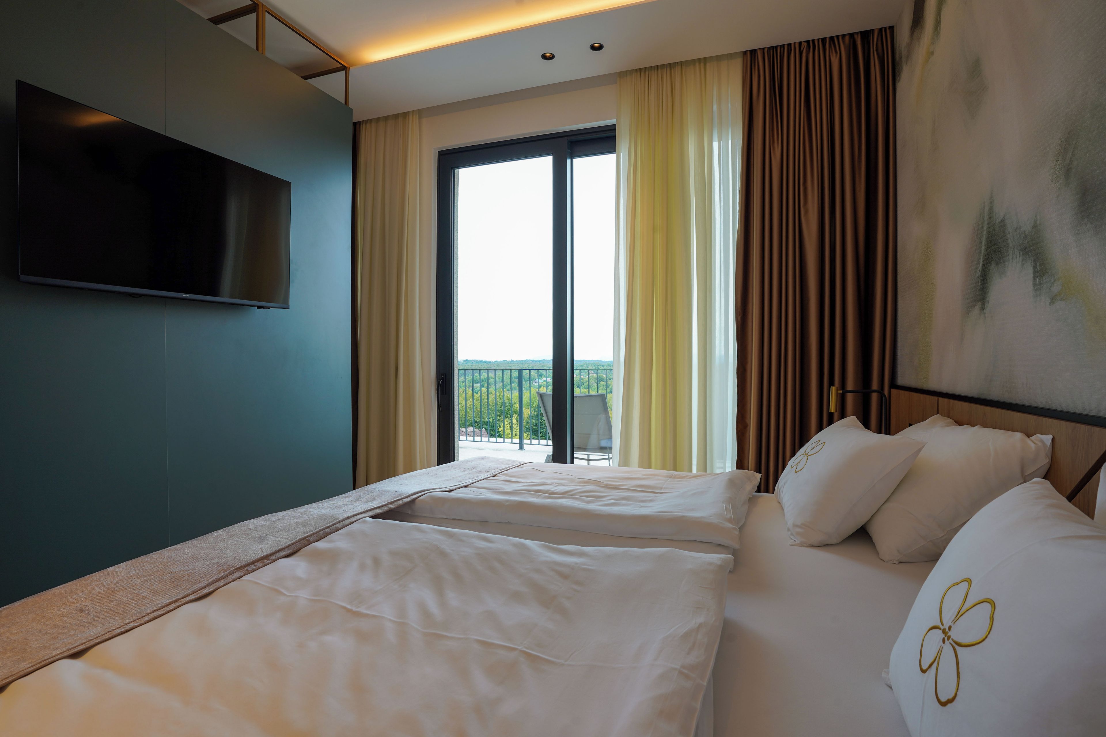 A hotel room with a bed, a TV, and a balcony with curtains.