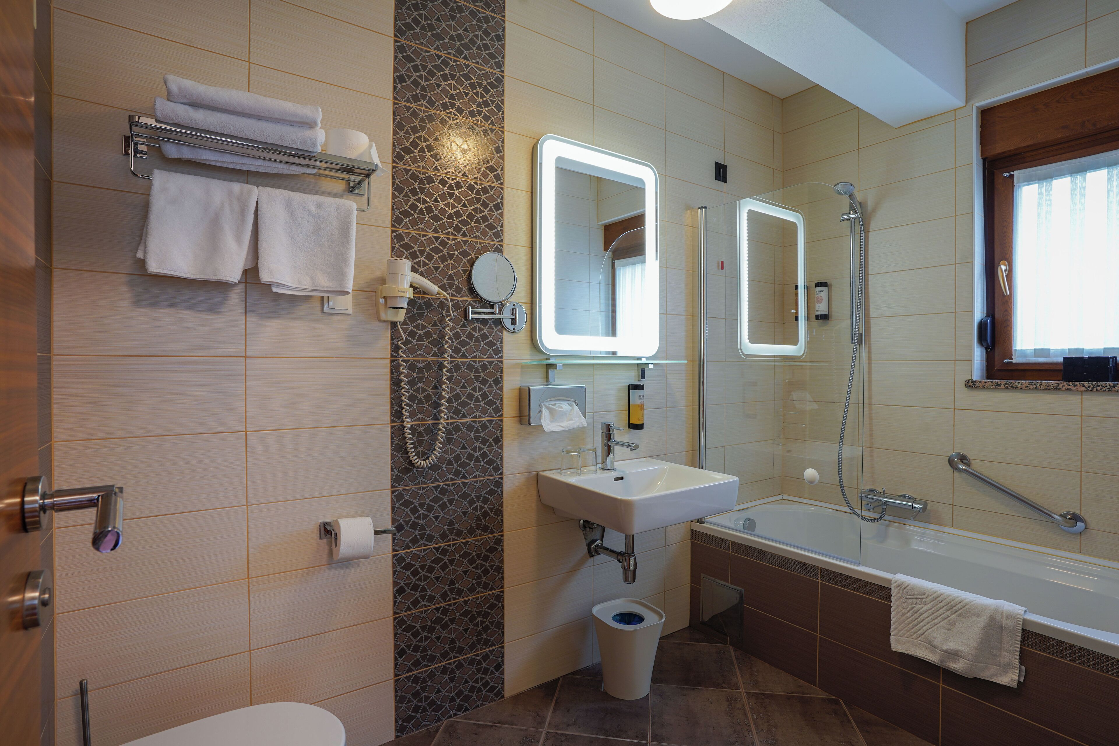A modern bathroom with a toilet, sink, and bathtub. There are towels on a rack and a mirror above the sink.