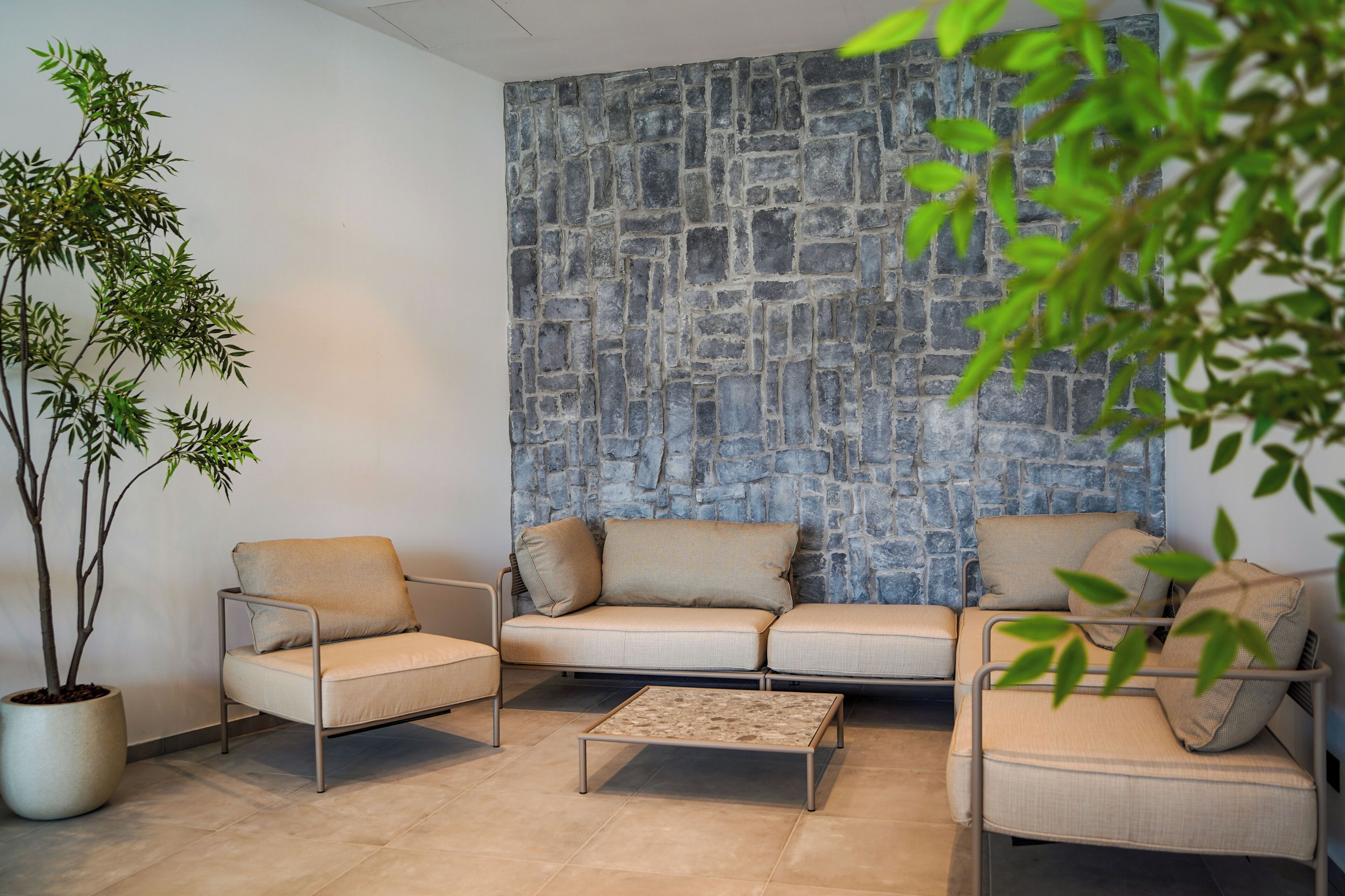 Una sala de estar moderna con una pared de acento de piedra, un conjunto de sofás, una mesa de centro y una planta en maceta.