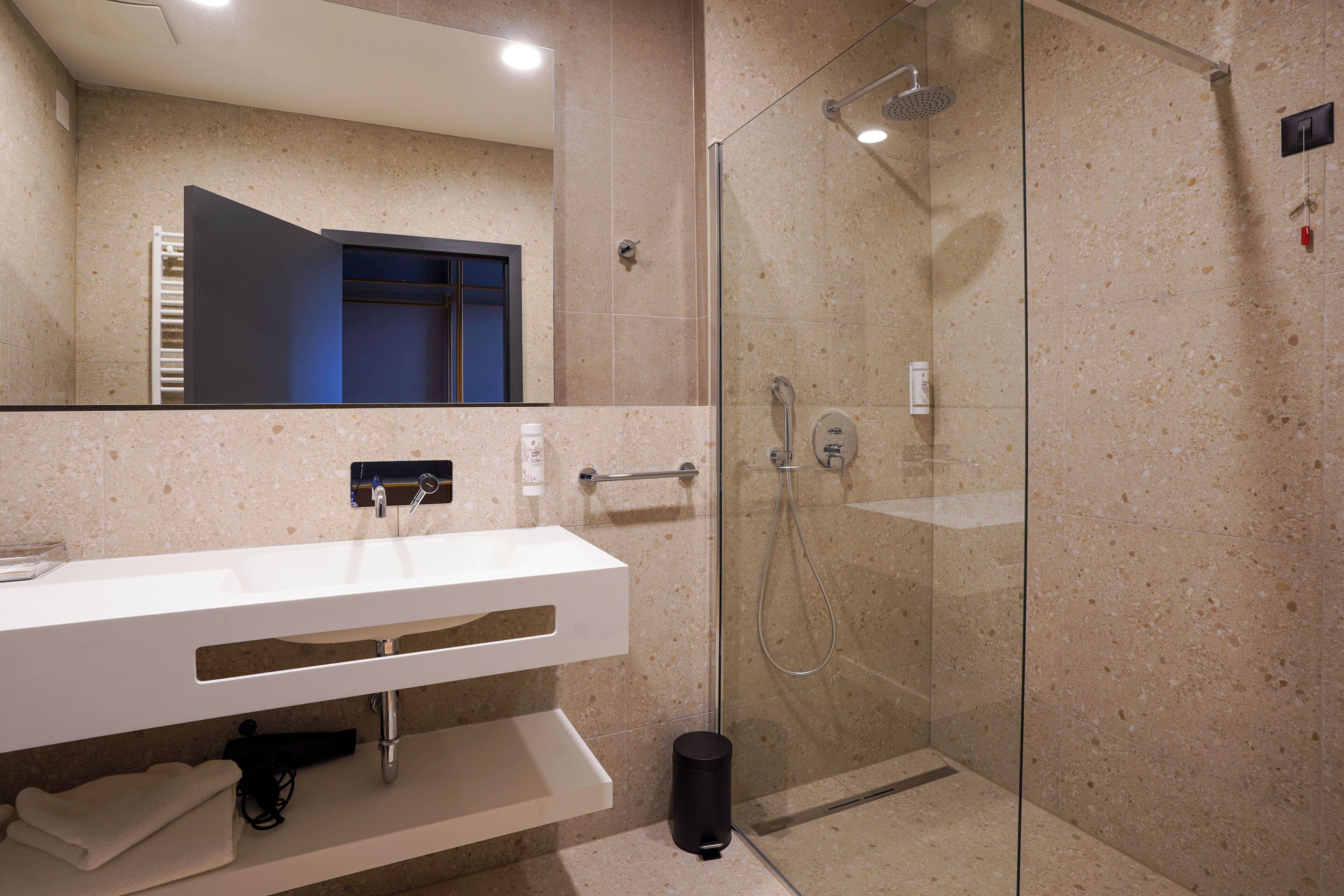 A modern bathroom with a glass-enclosed shower, a white sink with a towel rack, and a mirror above the sink.