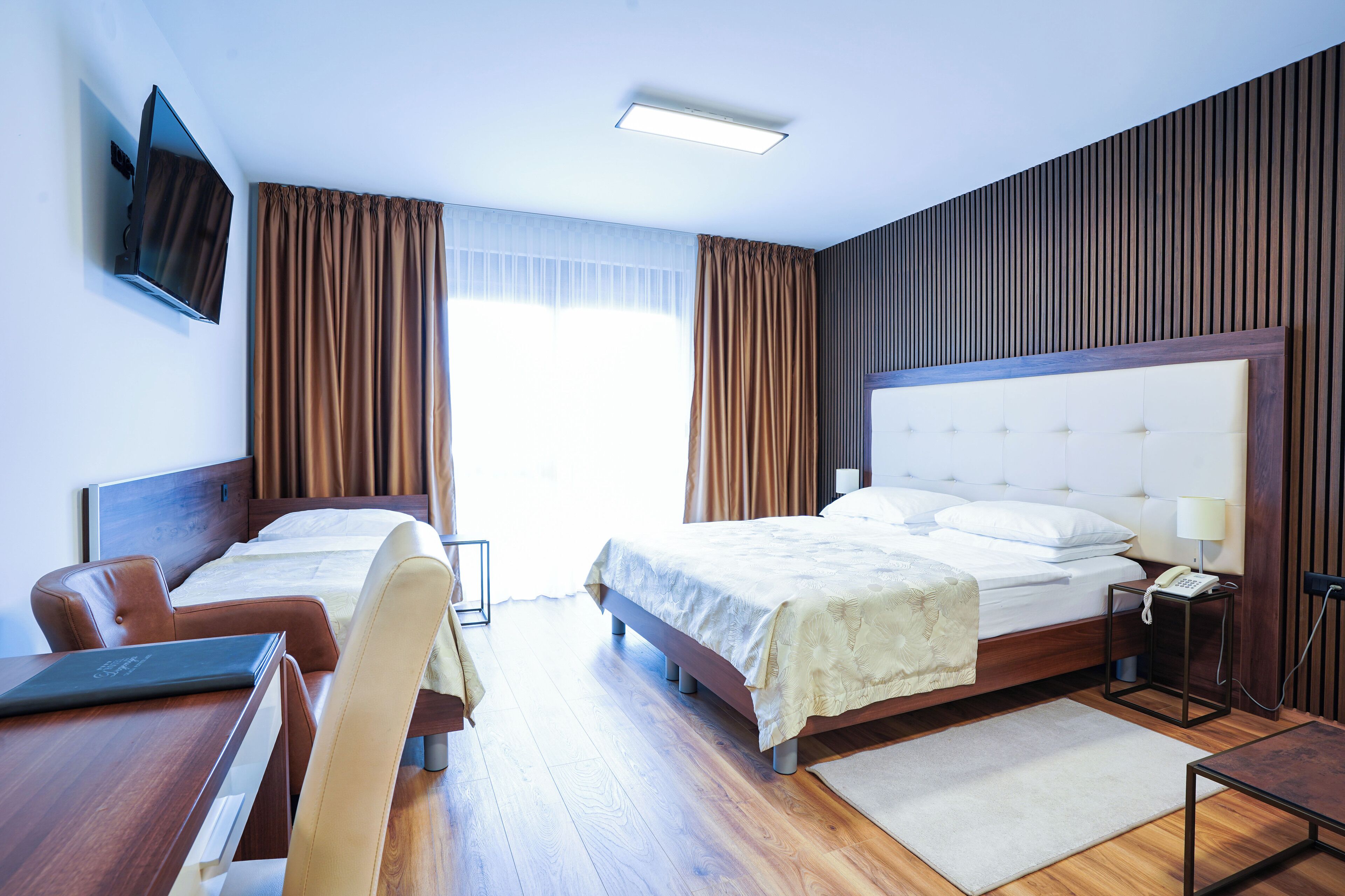 Hotellihuone, jossa on sänky, työpöytä tuolilla, seinälle asennettu televisio ja yöpöytä lampulla.