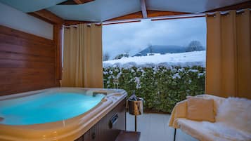 Una bañera de hidromasaje y un sofá en un espacio exterior cubierto con vistas a colinas nevadas.