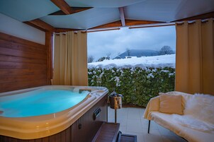 Una bañera de hidromasaje y un sofá en un espacio exterior cubierto con vistas a colinas nevadas.