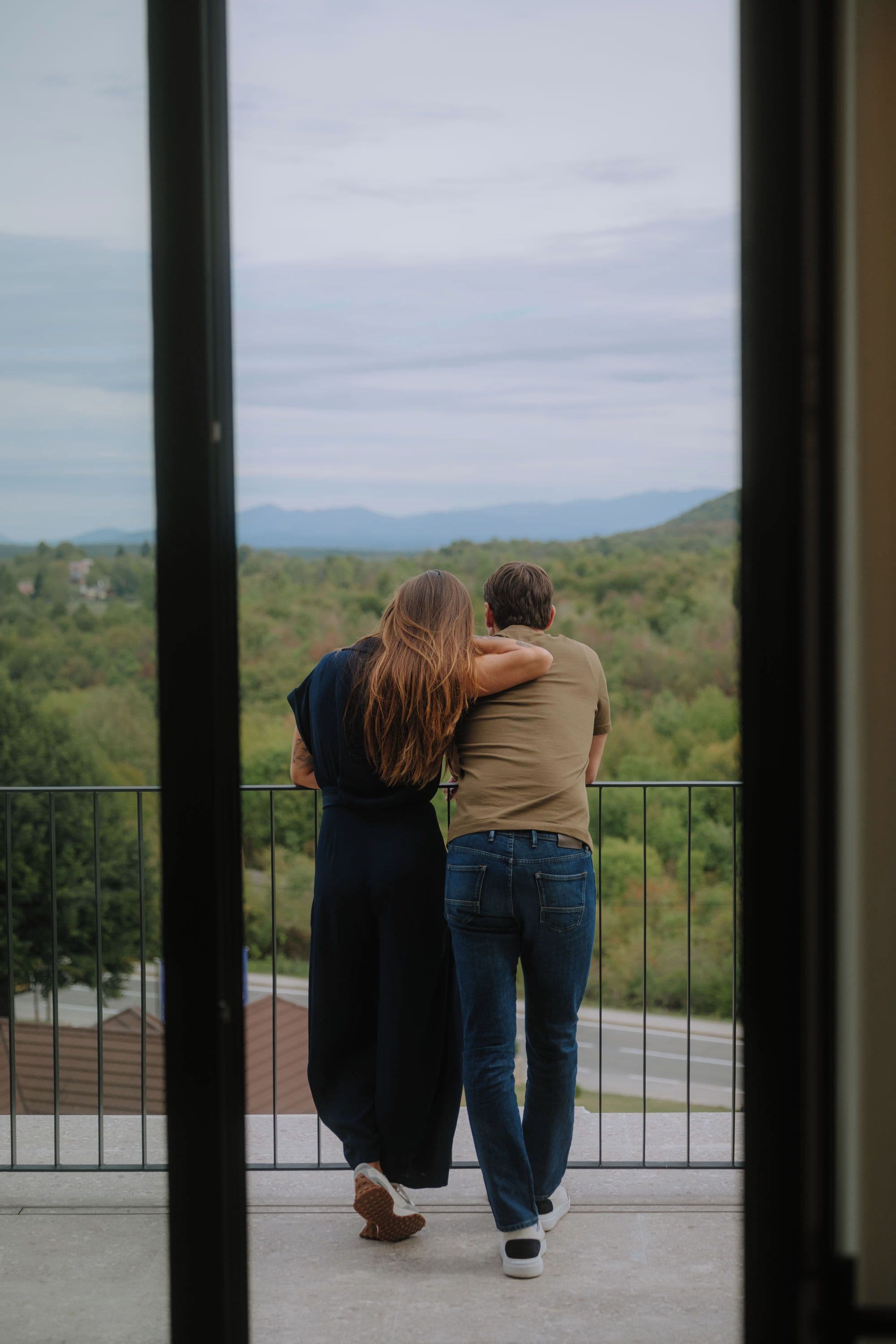 Un couple s’embrasse sur un balcon, avec une vue sur un paysage verdoyant.