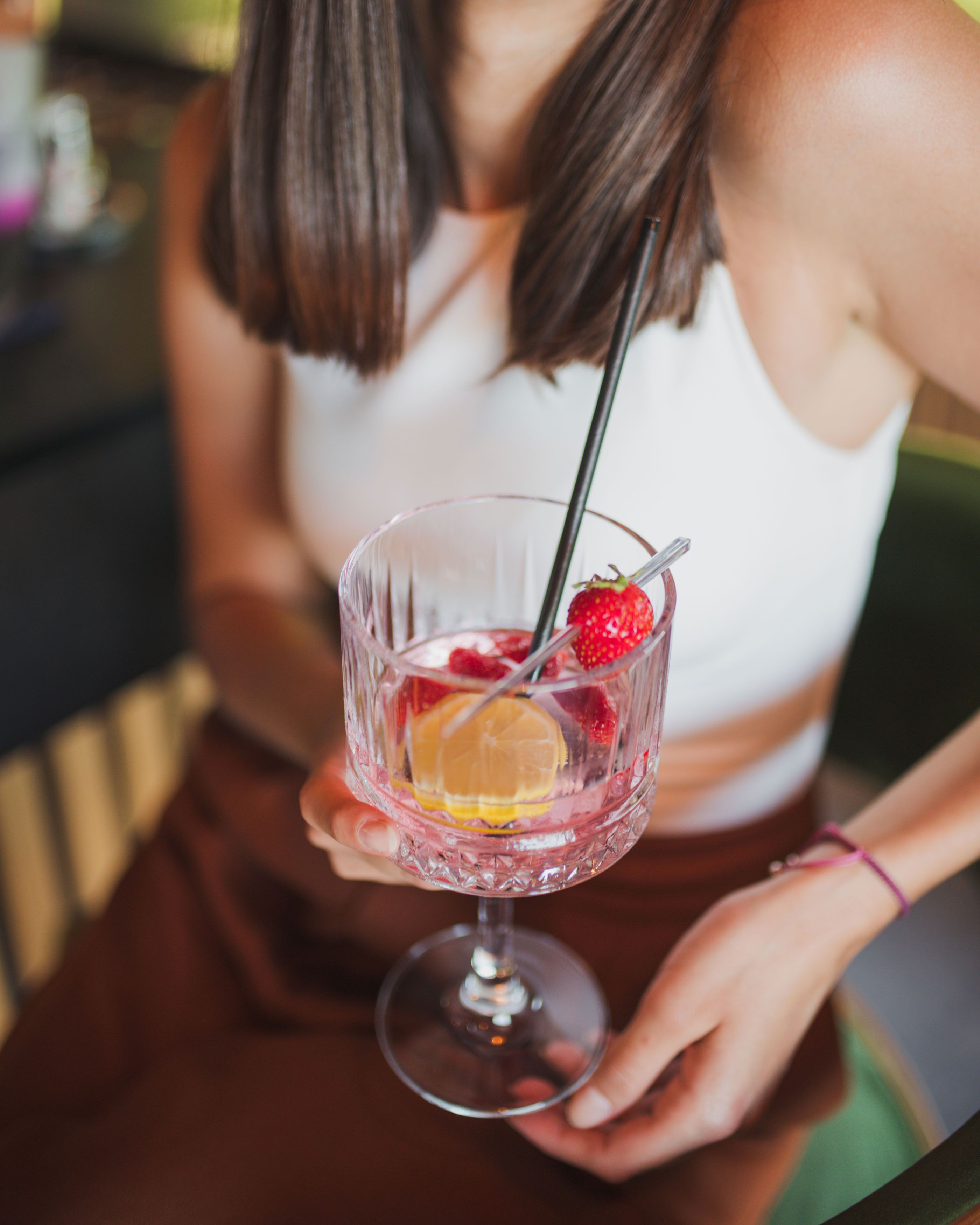 Una persona sosteniendo un vaso de cóctel con pajita, con una rodaja de limón, fresas y una bebida.