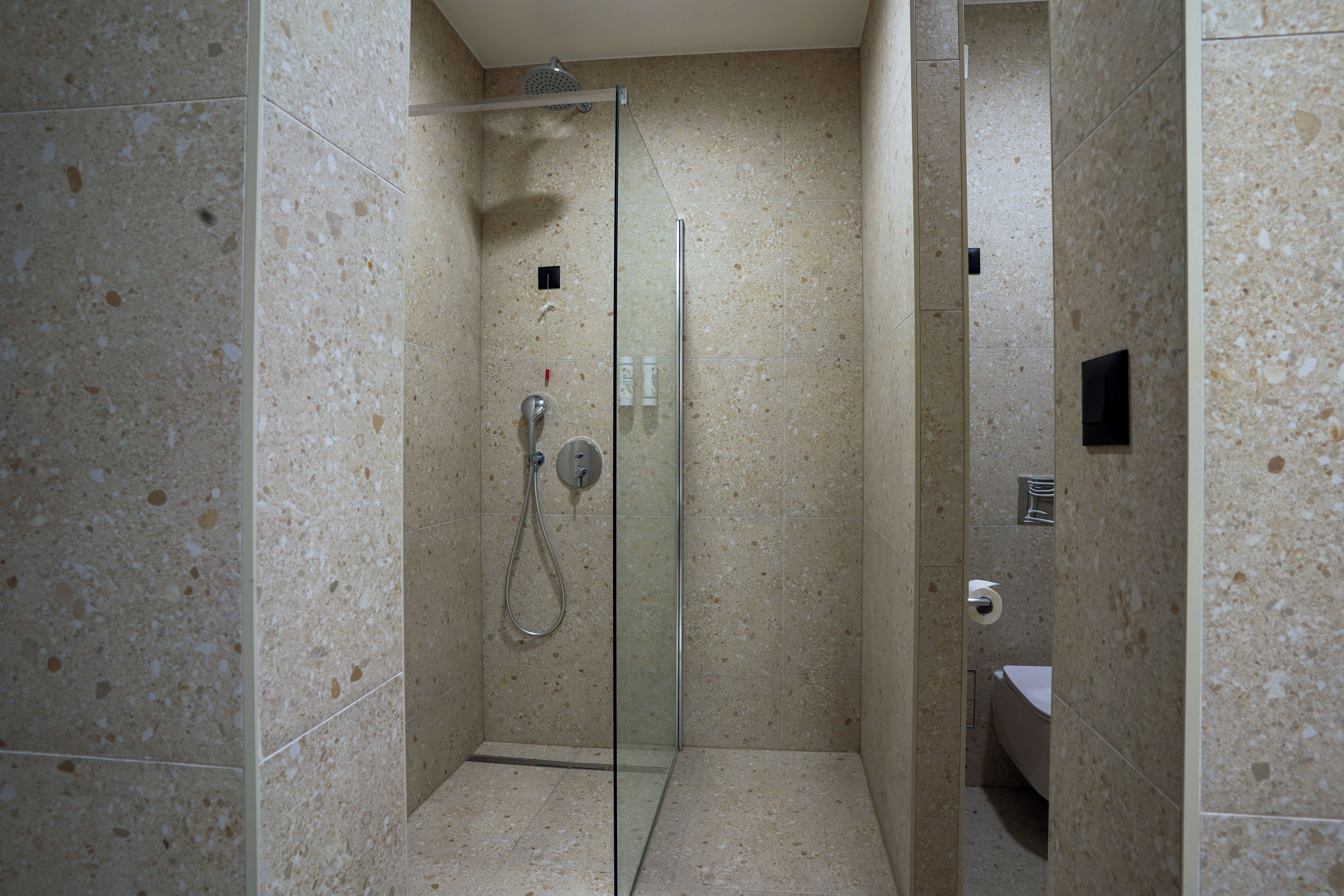 Eine gläserne Duschkabine mit Handbrause und am Wand montiertem Wasserhahn.