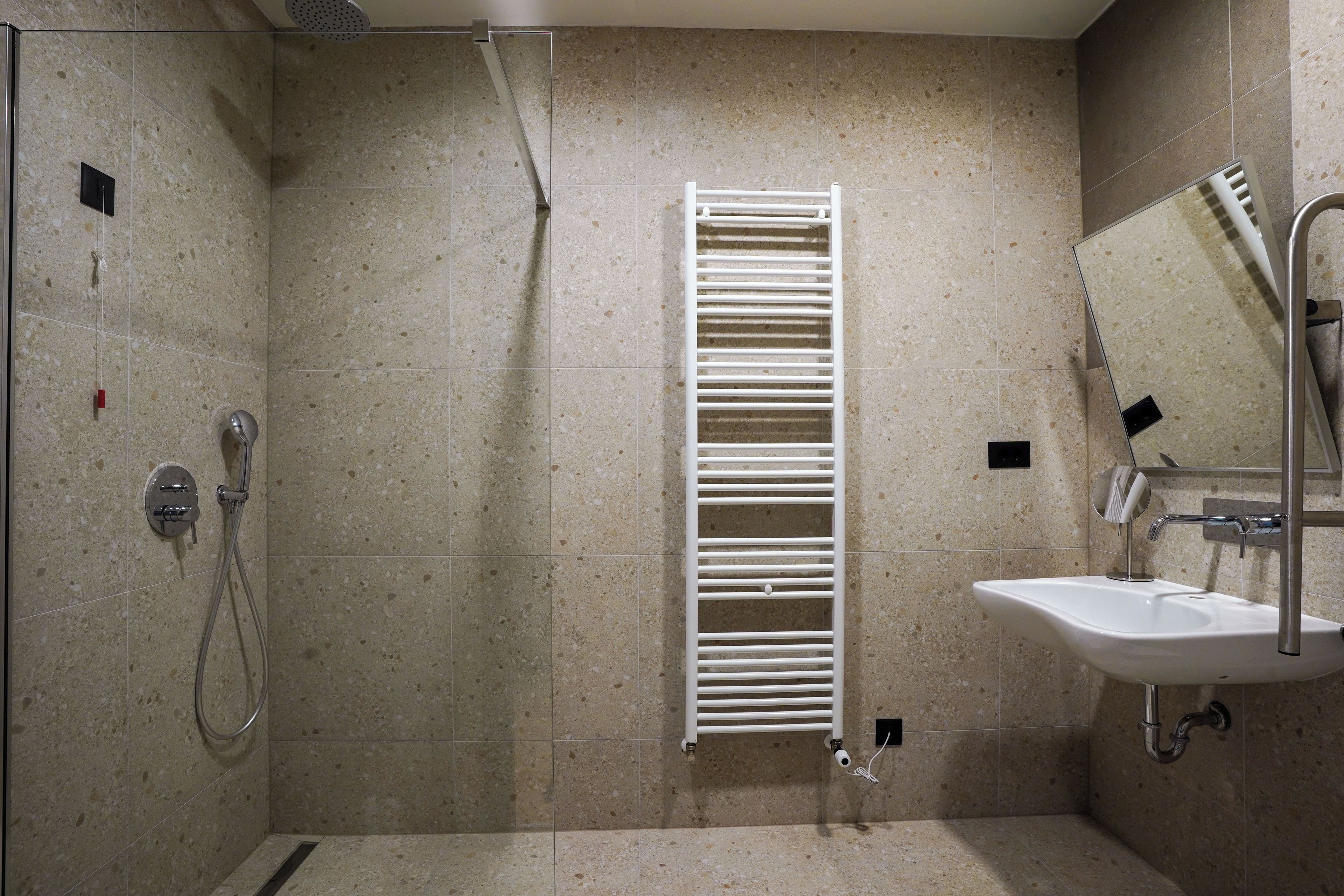 Casa de banho com chuveiro, um porta-toalhas branco, pia e espelho.
