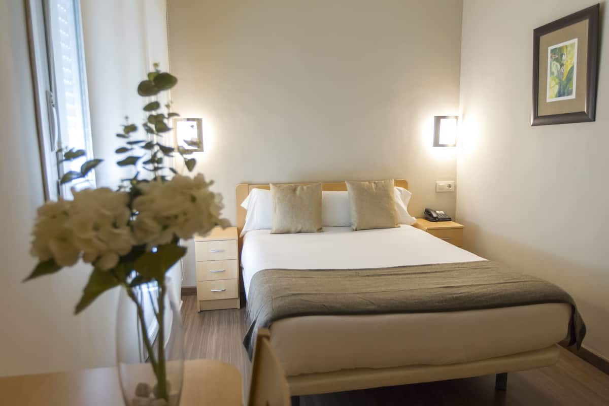 A hotel room with a bed, bedside tables, a vase with flowers, and a wall-mounted phone.