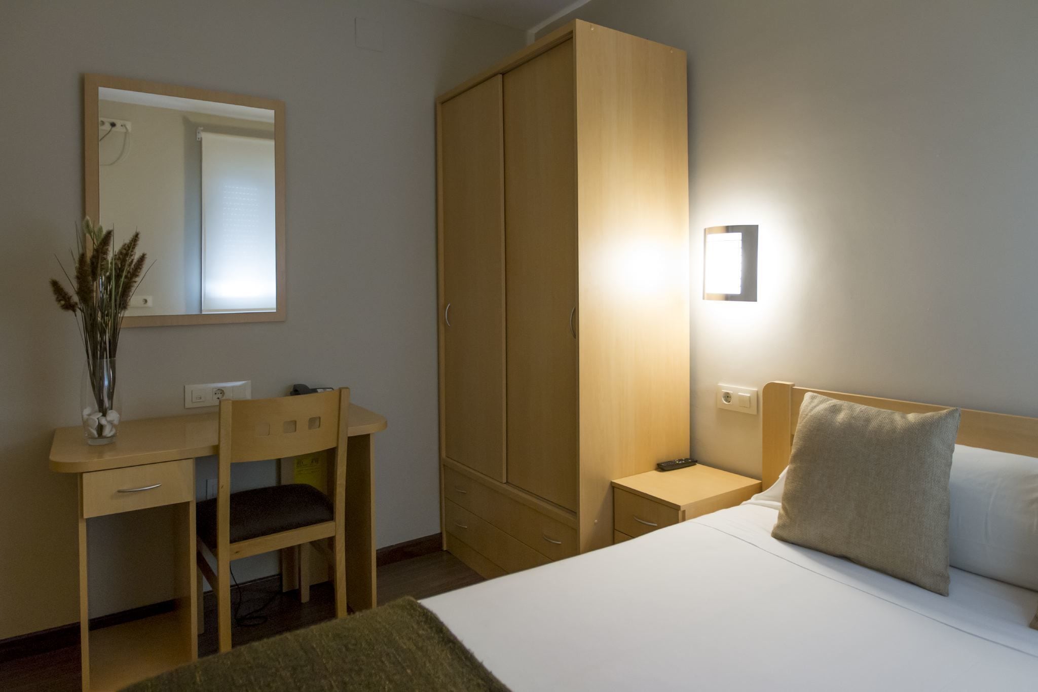 Une chambre à coucher comprenant un lit, une table de chevet, une commode, un bureau avec une chaise, une armoire et un miroir.