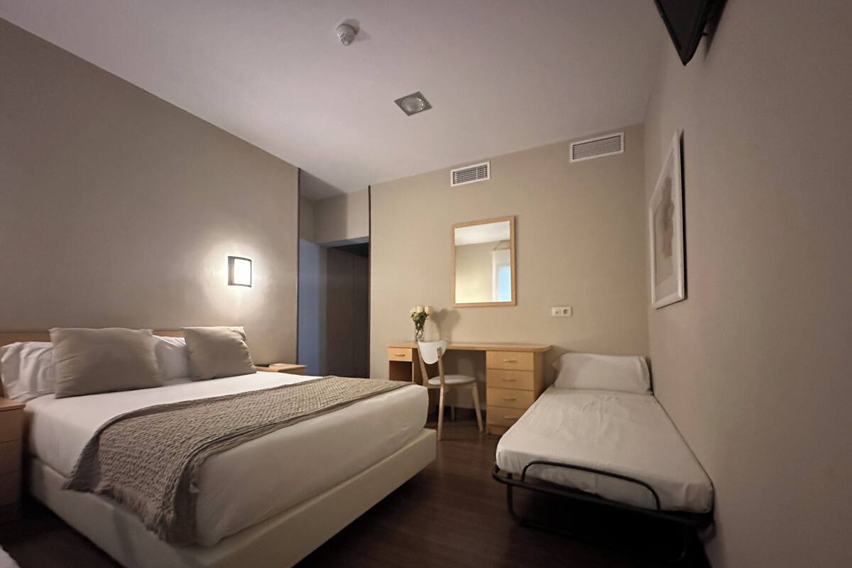 A hotel room with a large bed, a smaller bed, a desk, and a chair.