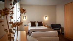 A modern bedroom with a bed, bedside tables, a chair, and a wooden wardrobe. - Hotel Vettonia (Merida)