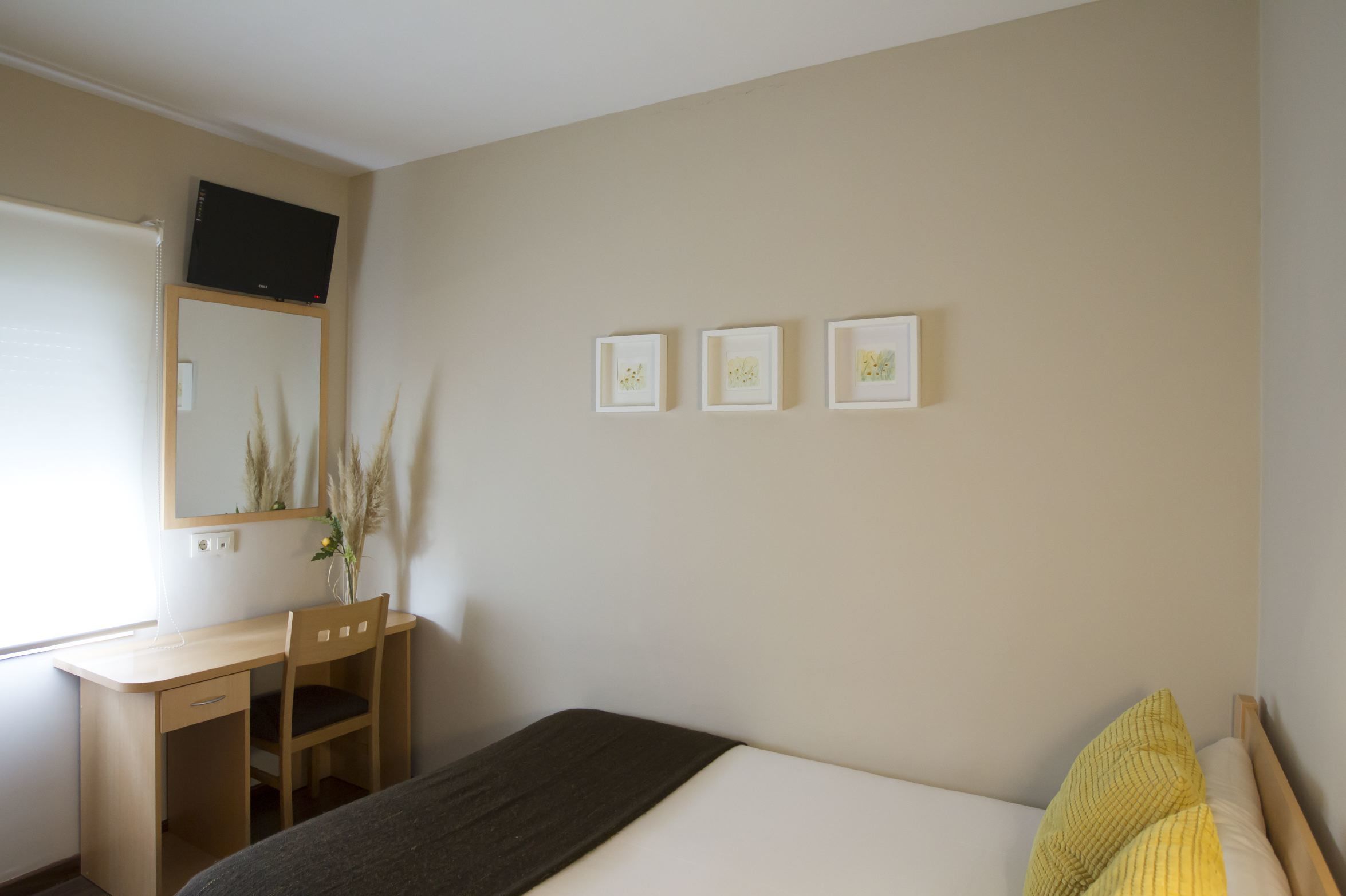 Quarto com cama, escrivaninha e cadeira. Há três quadros na parede.