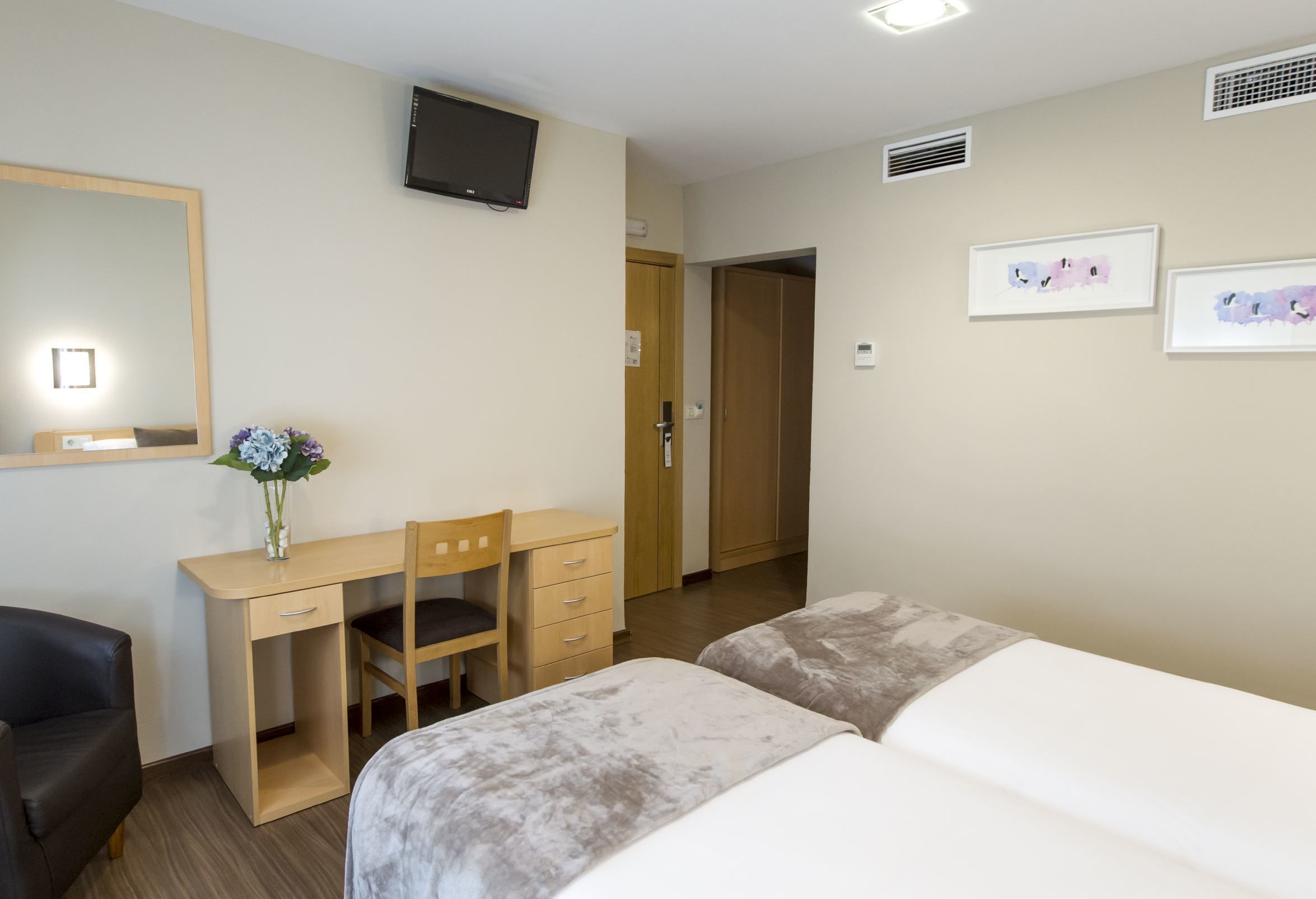 Une chambre d’hôtel équipée d’un lit, d’un bureau, d’une chaise, d’une télévision et d’œuvres d’art accrochées au mur.