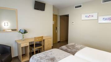 Una habitación de hotel con cama, escritorio, silla, televisor y obras de arte en la pared.