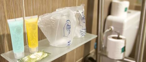 Artículos de aseo en un estante de baño, incluyendo una pastilla de jabón verde, una loción amarilla y una bolsa blanca con un diseño azul.