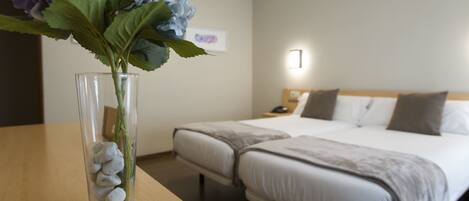 A hotel room with a bed, bedside table, and a vase with flowers.