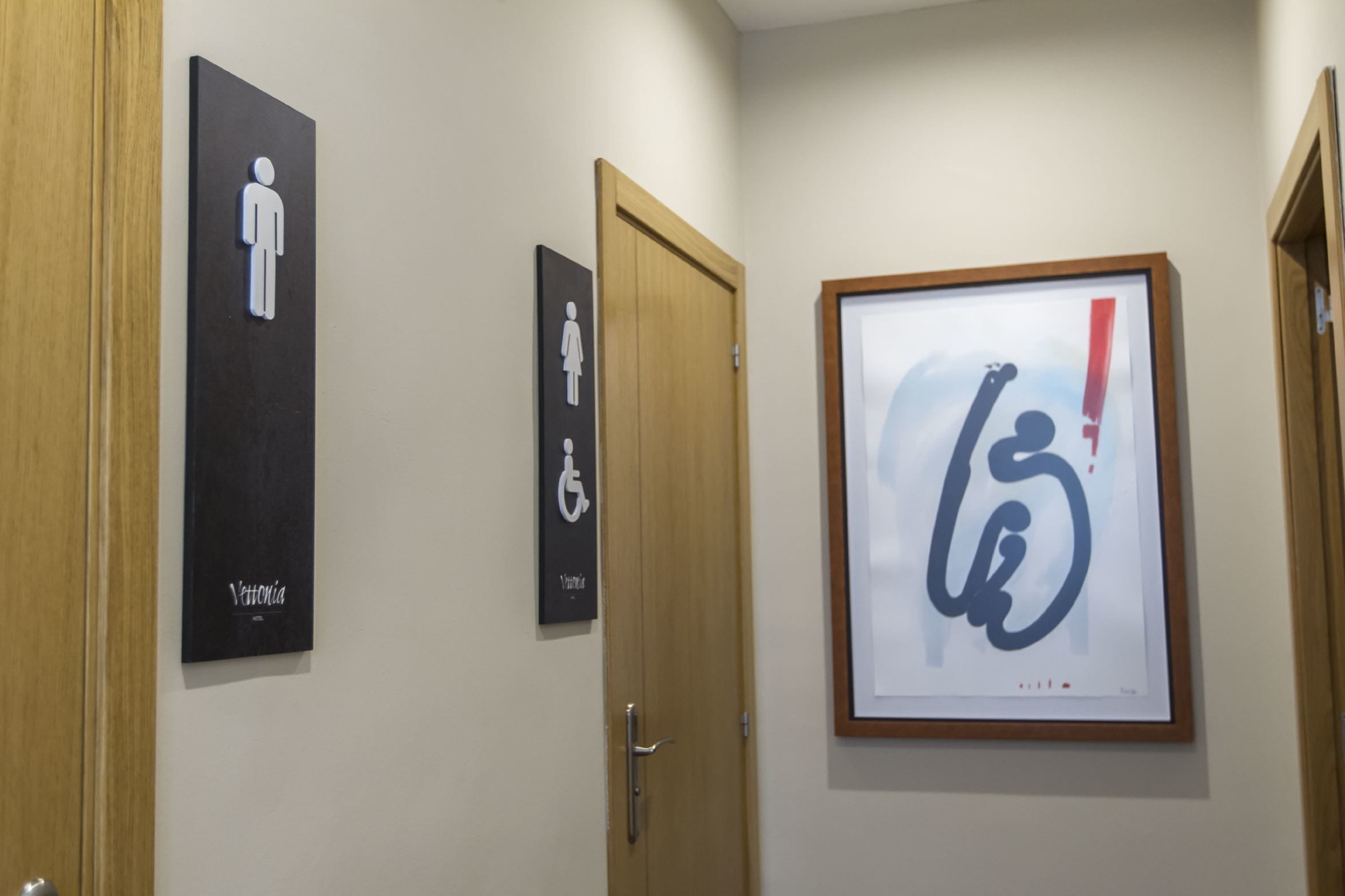 Un pasillo con tres letreros: baño para hombres, baño para mujeres y baño accesible para sillas de ruedas.