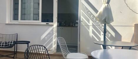 Un balcón con mesa y sillas, una puerta corrediza de vidrio y vista a la cocina.