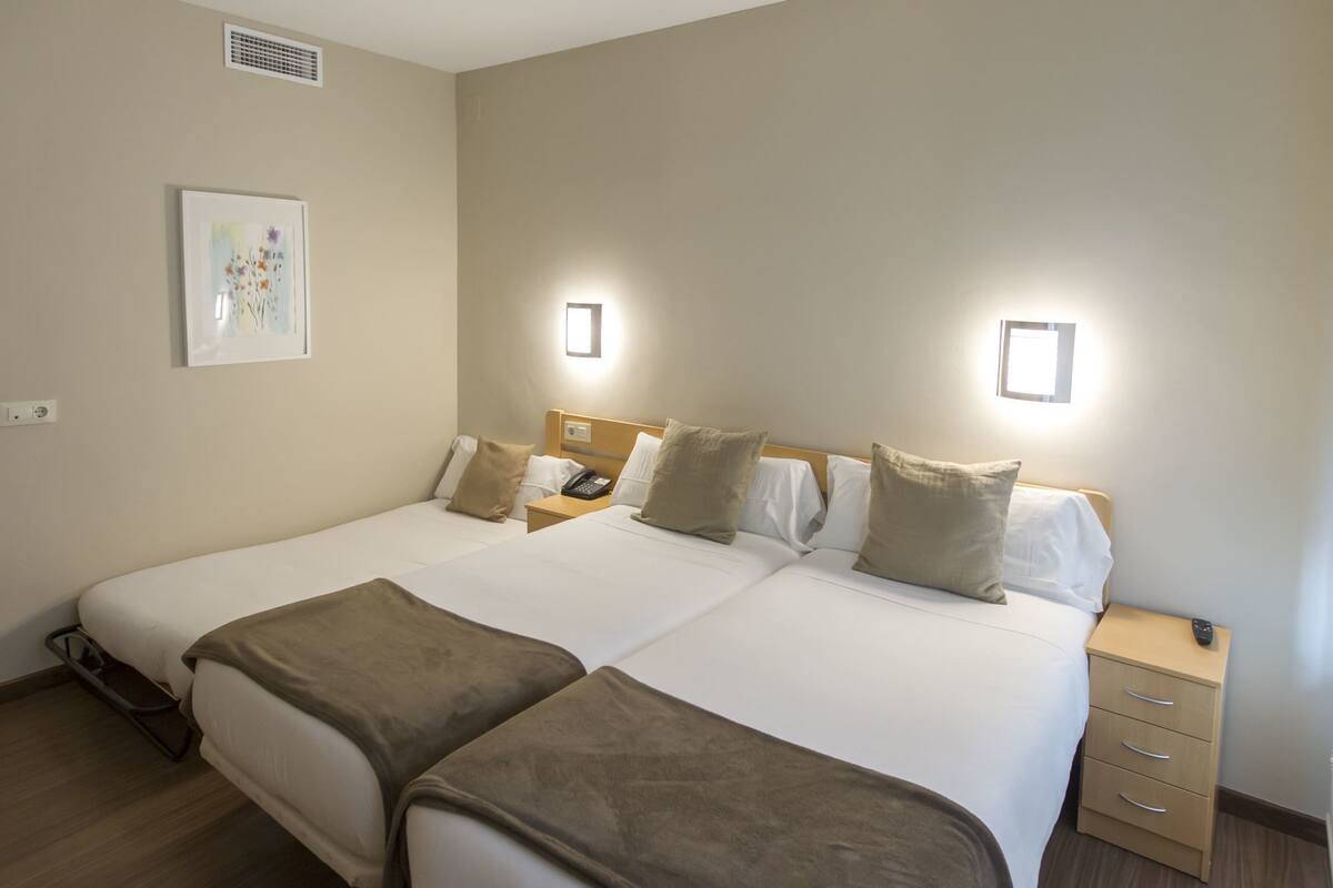 A double bed with a bedside table, a nightstand, a phone, and a wall-mounted light fixture.