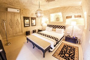 A bedroom with a large bed, a bench, a patterned rug, a chandelier, and a wall-mounted mirror. - Hezen Cave Hotel (Ürgüp)