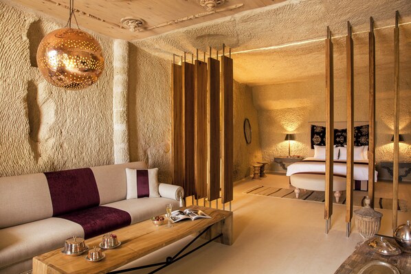 A modern hotel room with a sofa, a wooden coffee table, and a bed with a white headboard. - Hezen Cave Hotel (Ürgüp)
