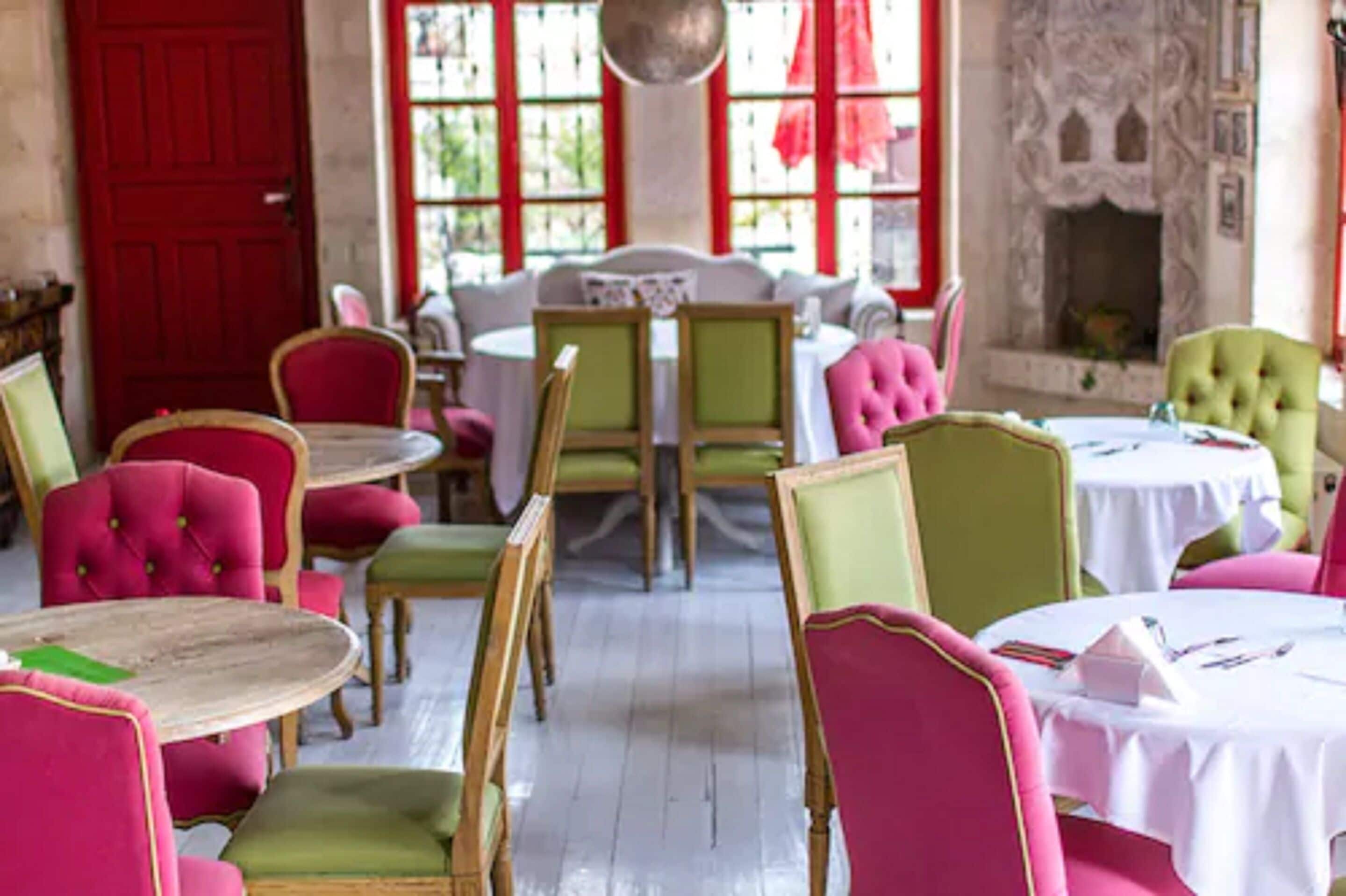Un comedor con mesas y sillas redondas, una puerta roja y una chimenea.