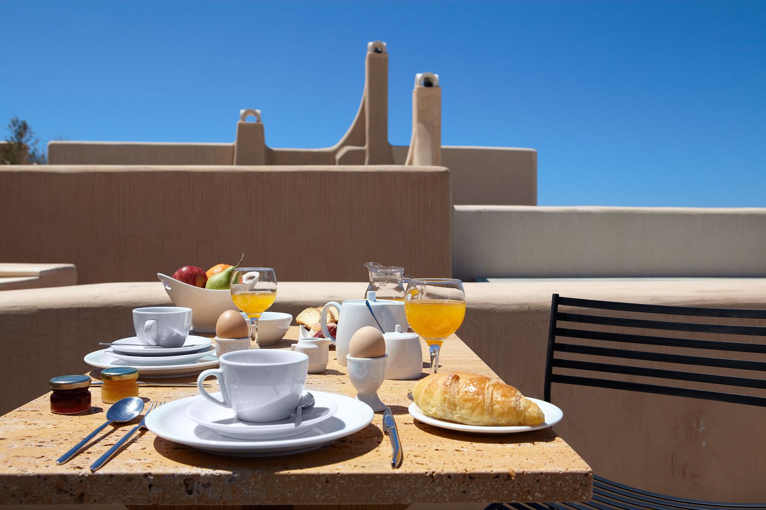 Ein Frühstückstisch auf einer Terrasse mit Blick auf ein modernes Gebäude im Hintergrund.
